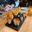 Several metal cups of French fries and dipping sauces sit on a wooden tray on a dining table.