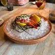 Four shrimp topped with red sauce and white shavings sit on crushed ice with lemon wedges and strands of seaweed.