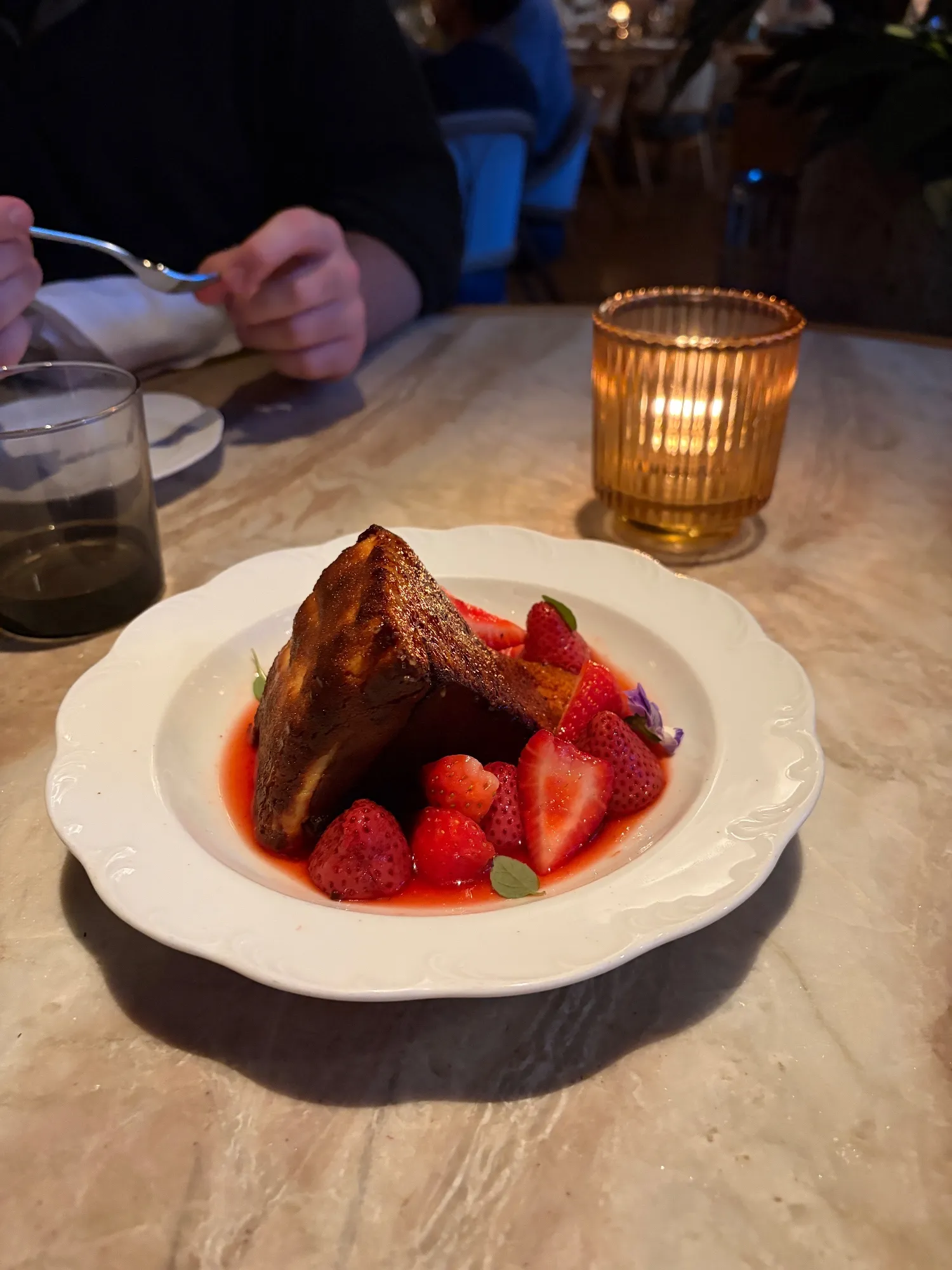 A wedge of cheesecake with a browned top sits in red berry sauce with strawberries.