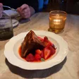 A wedge of cheesecake with a browned top sits in red berry sauce with strawberries.