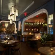 A dining room contains set tables, booths, arched openings, hanging lights and plants.