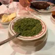 A bowl of creamed spinach with a spoon, a dish of butter behind it and a steak on a plate in the background.
