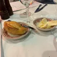 A roll of bread with sesame on a plate with a knife, beside a dish of butter and wine glasses.