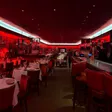 A red-lit dining room with white-tablecloth tables, framed pictures covering the walls, and a bar along one side.