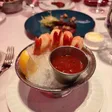 Shrimp arranged over crushed ice around a metal cup of cocktail sauce, with a lemon wedge at the side.