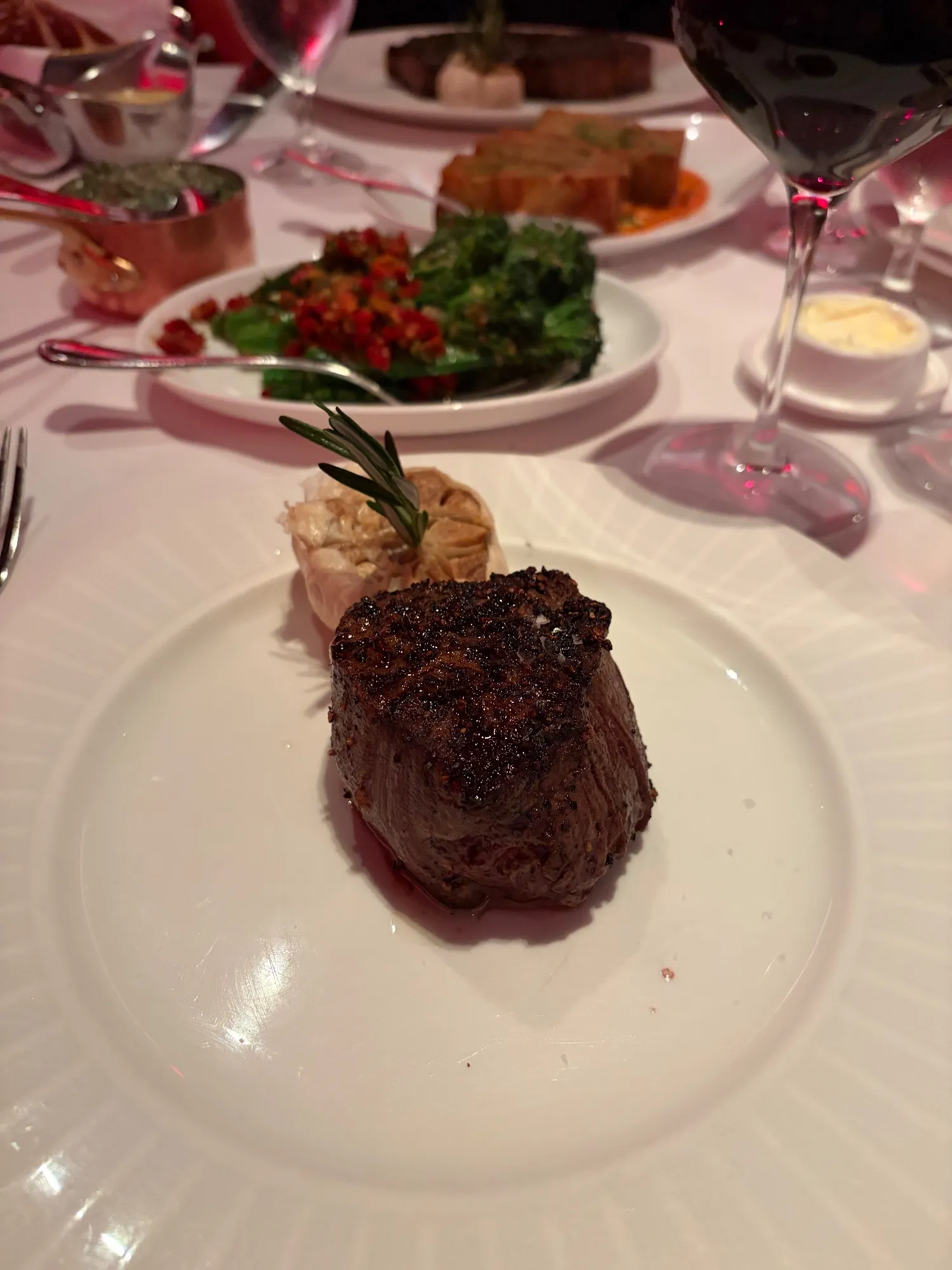 A barrel-cut filet on a white plate with a roasted garlic bulb and rosemary sprig behind it.