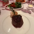 A barrel-cut filet on a white plate with a roasted garlic bulb and rosemary sprig behind it.