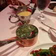 Creamed spinach in a copper pan with a serving spoon, surrounded by other dishes and sauce boats.